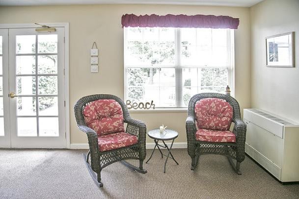 A cozy living room corner featuring two wicker chairs with red cushions and a small side table by the window.