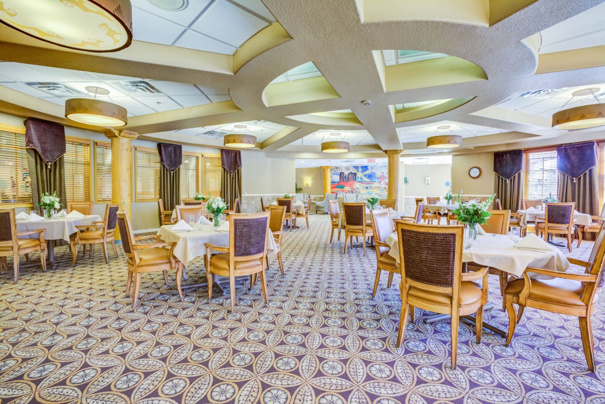 An elegant dining room with beautifully arranged tables and chairs, featuring floral decorations and ambient lighting.