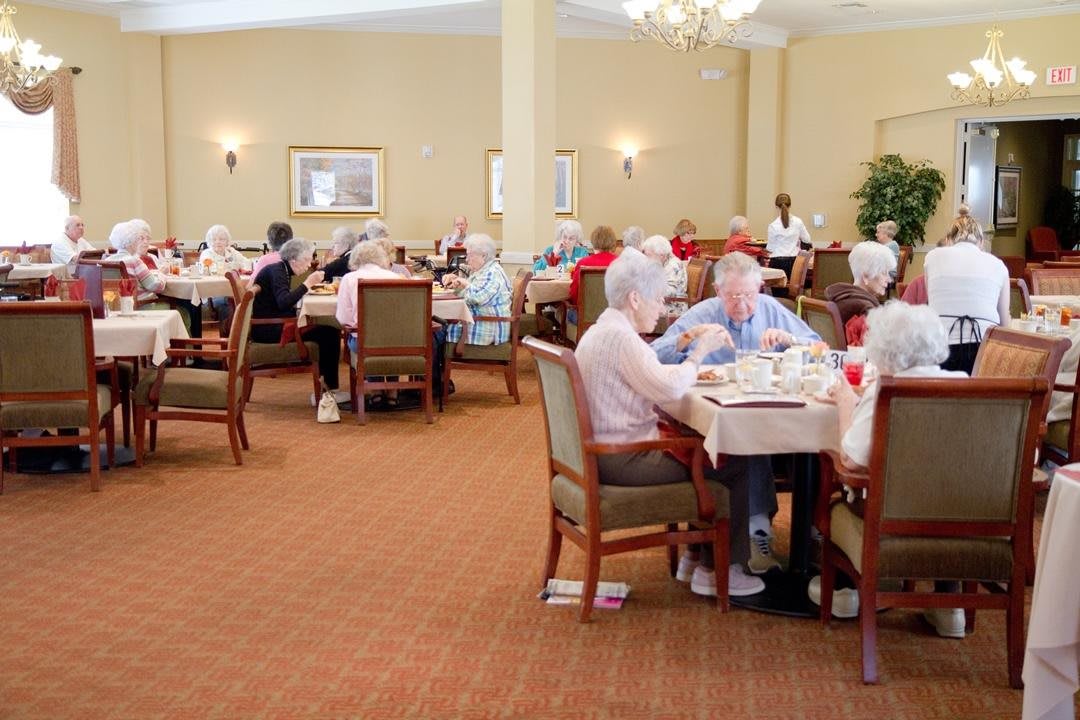 Elderly residents enjoying a meal together in a senior living dining room.