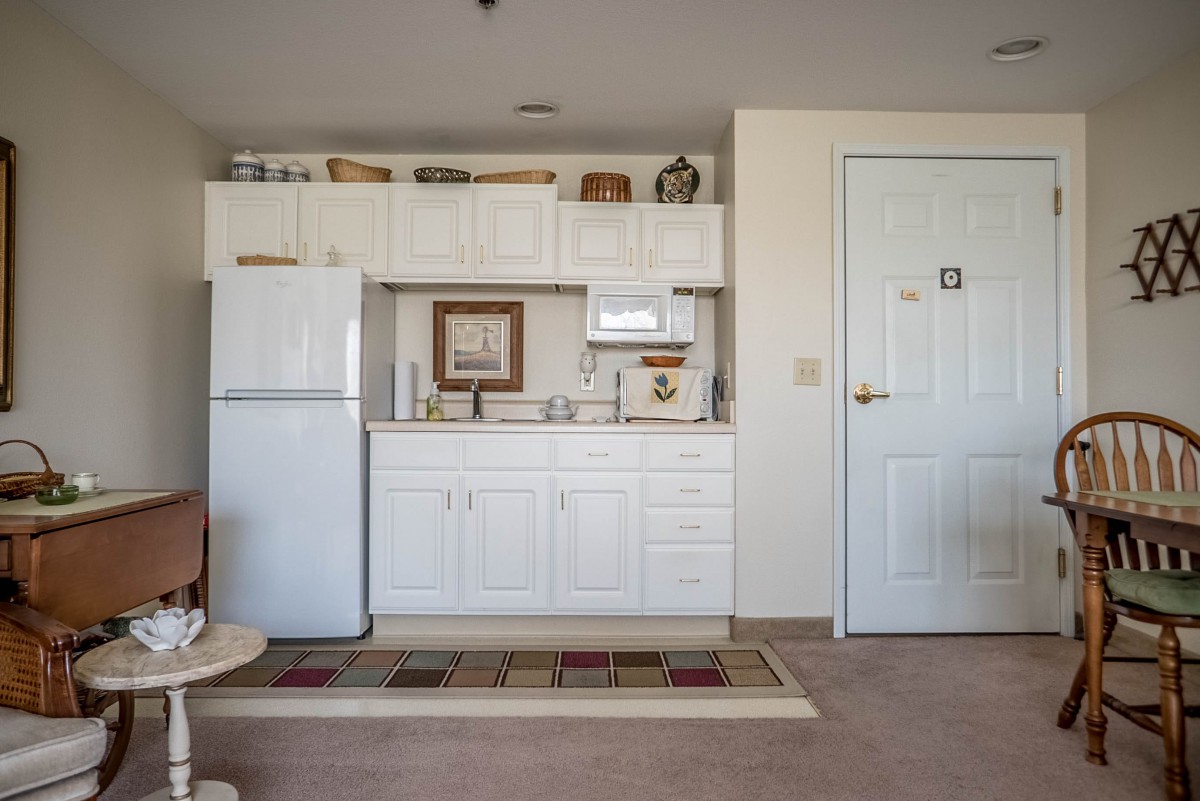 A compact kitchen area in an apartment with white cabinets and appliances.