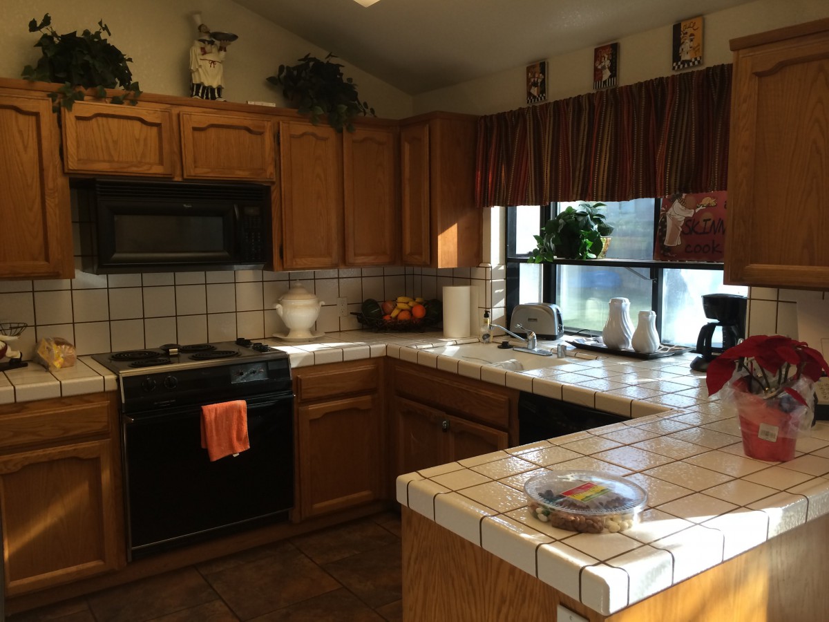 A cozy kitchen with wooden cabinets, tiled countertops, and various appliances.