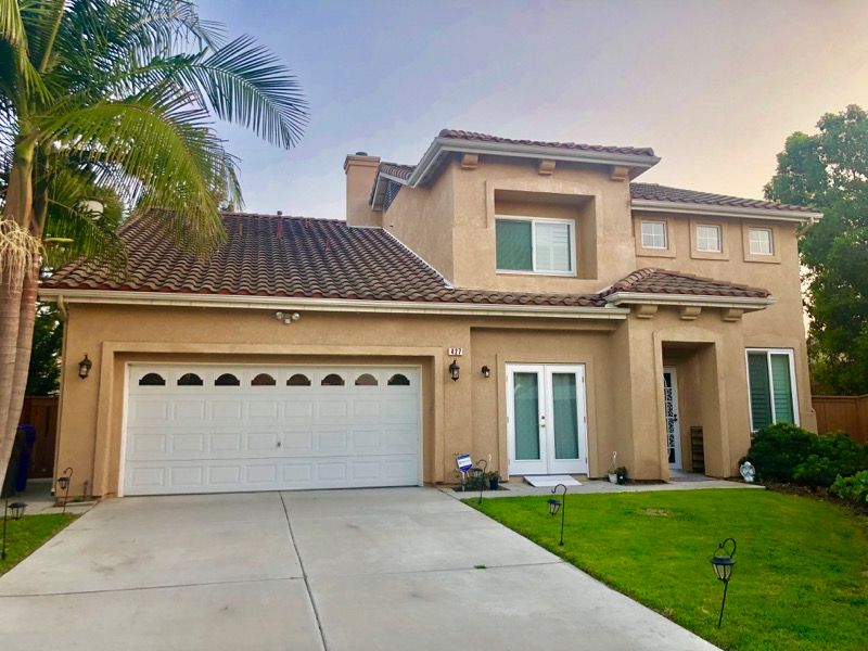 A two-story house with a garage, green lawn, and a palm tree at sunset.