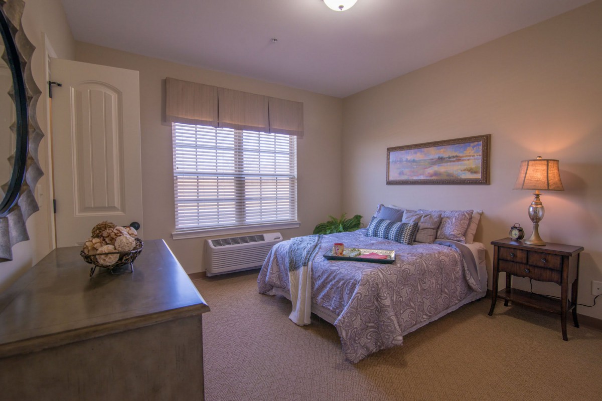 A cozy bedroom with a neatly made bed, large window, and wall artwork.