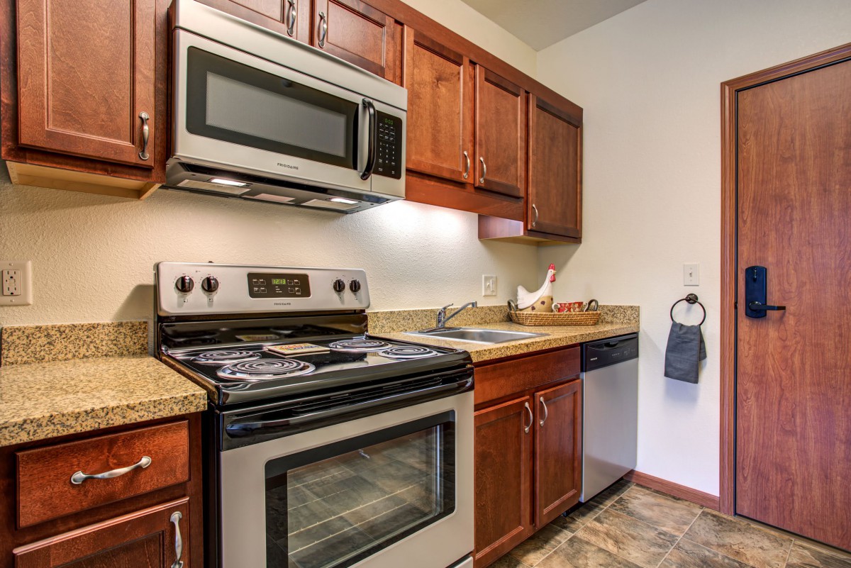 A modern kitchen with wooden cabinets, featuring an oven, microwave, sink, and dishwasher.