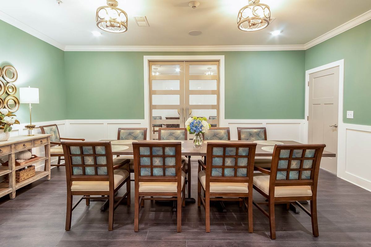 A spacious dining room with a large table surrounded by wooden chairs, featuring elegant lighting and green walls.