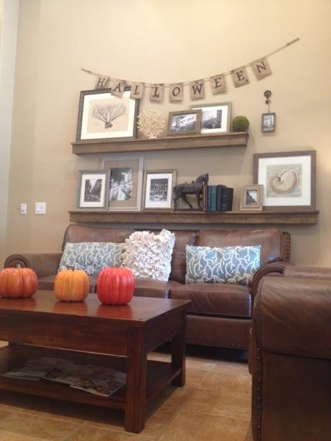 A cozy living room decorated with fall-themed elements like pumpkins and a 'welcome' banner on the shelves.