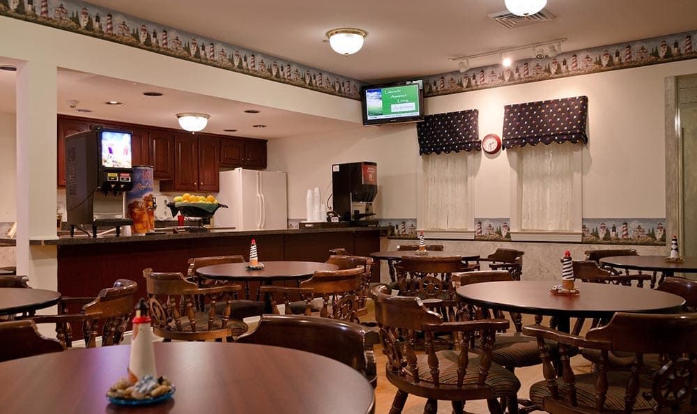 A cozy dining area with wooden tables and chairs, a television, and an open view of the kitchen.