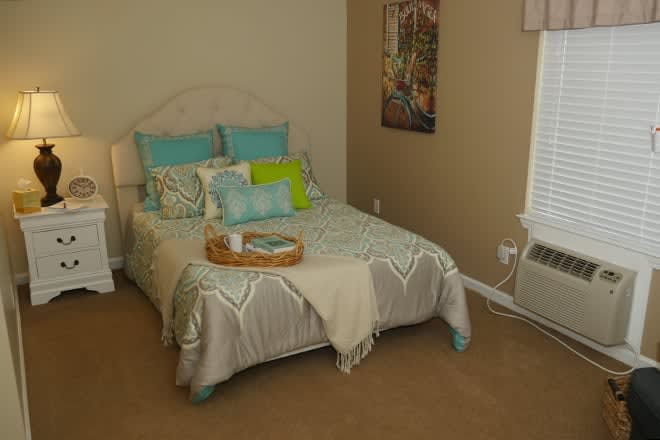A cozy bedroom with a neatly made bed featuring blue and green pillows, a decorative tray, and a poster on the wall.