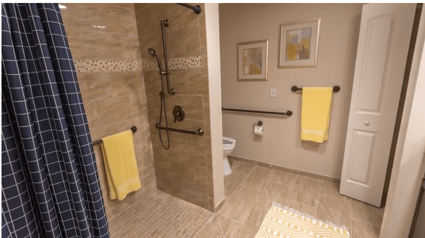 A modern and accessible bathroom with a walk-in shower, grab bars, and yellow towels.