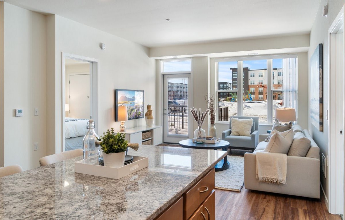 A modern open-plan living room and kitchen with contemporary furnishings and a view of an outdoor area.