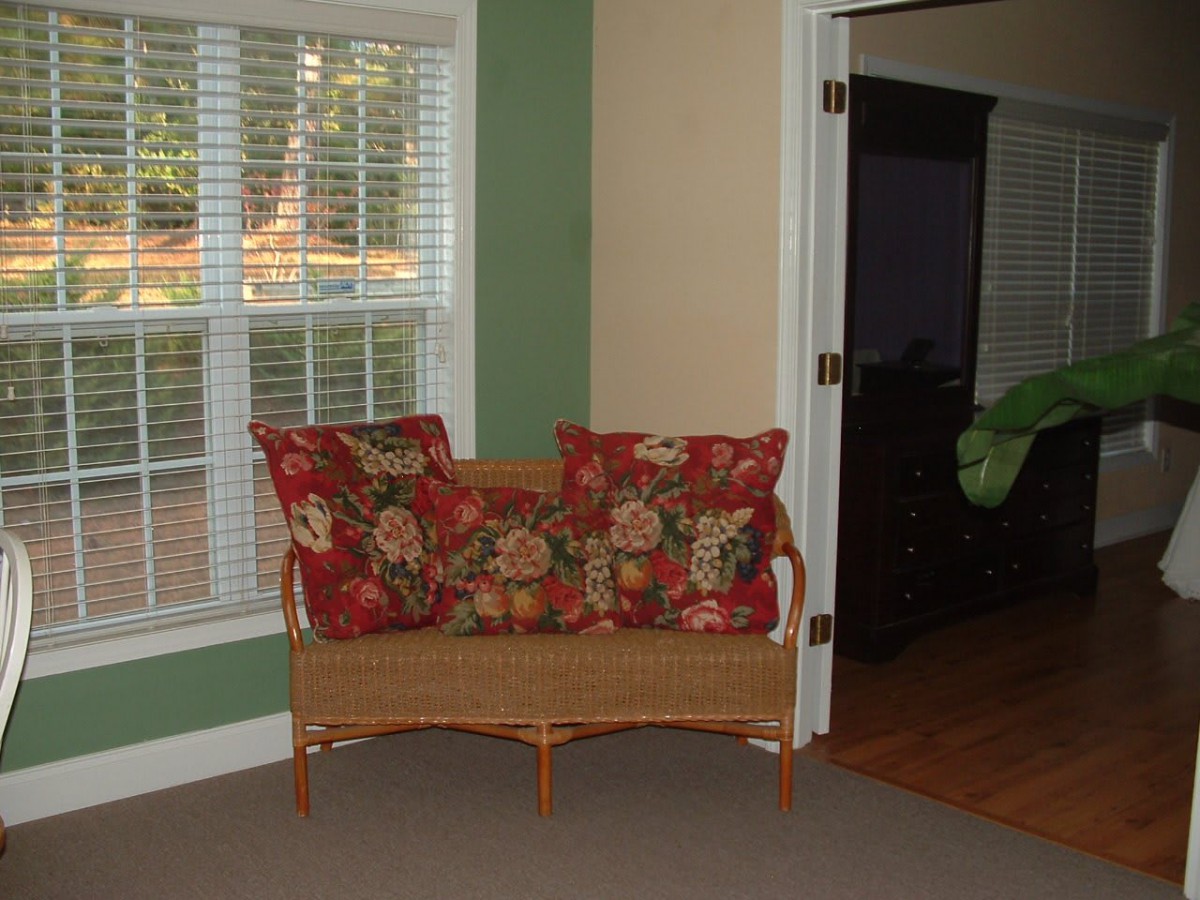 A cozy living room corner featuring a wicker loveseat with floral-patterned pillows beside a window.