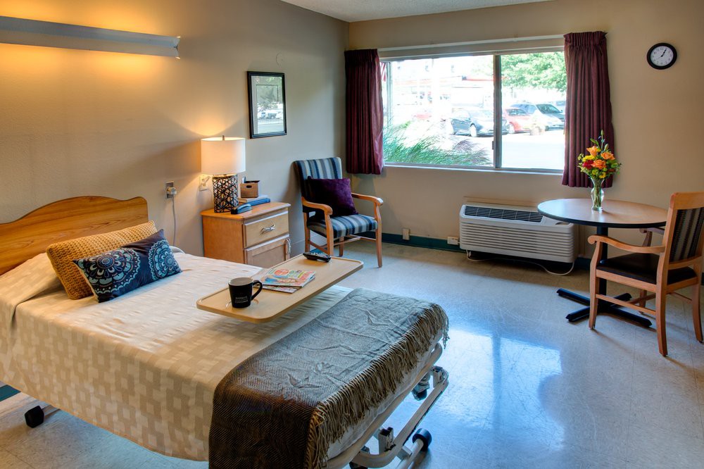 A well-lit hospital room with a bed, chair, and window.