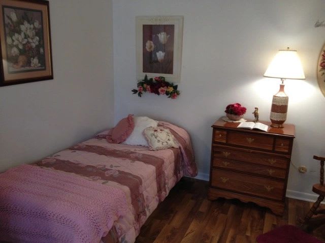 A cozy bedroom with a single bed, wooden dresser, and a lamp providing warm lighting.