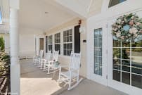 A cozy porch with white rocking chairs and large windows.