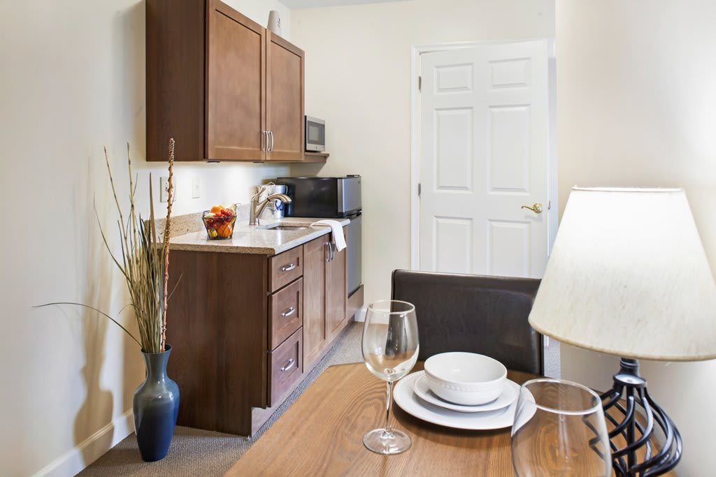 A cozy kitchen and dining area featuring wooden cabinets, a microwave, and a neatly set table with plates and glasses.
