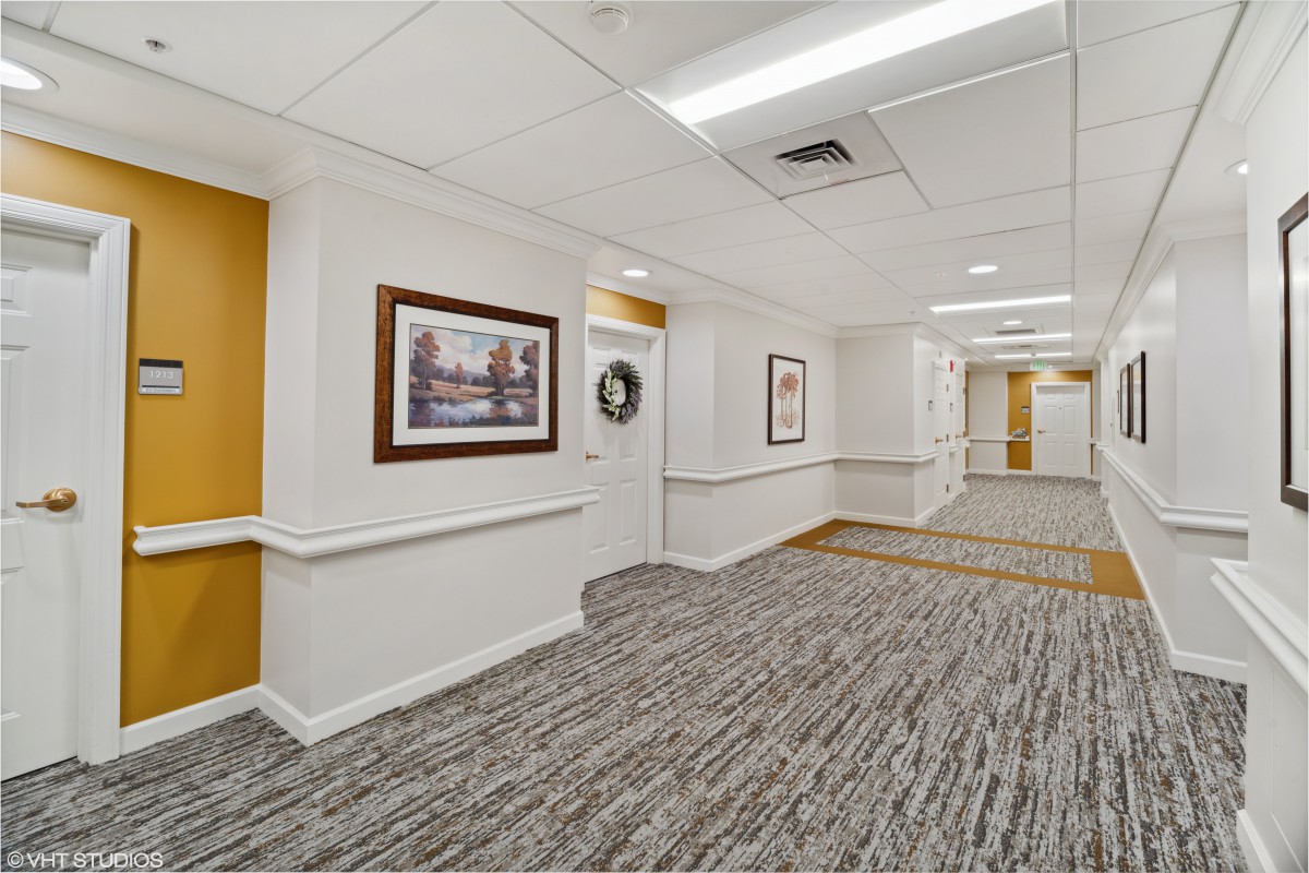 A well-lit hallway with carpeted flooring and framed artwork on the walls.