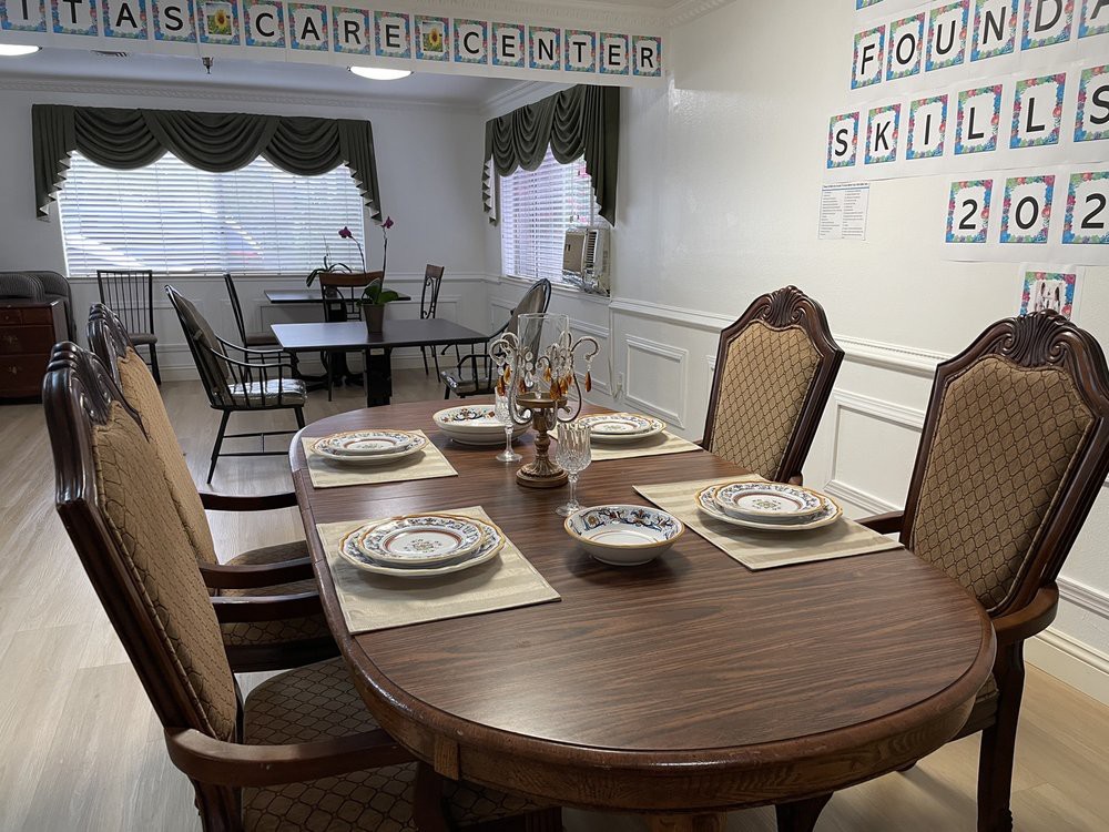 A neatly set dining room table with plates and cutlery, surrounded by chairs, in a well-lit interior space.