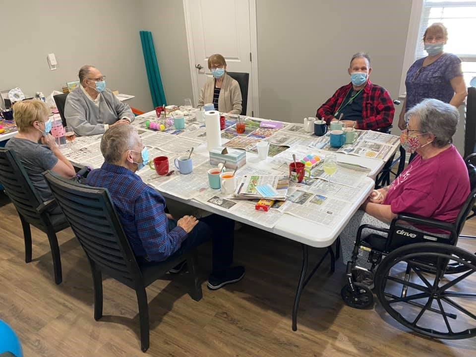 A group of seniors sitting around a table, engaging in a social meeting while wearing masks.