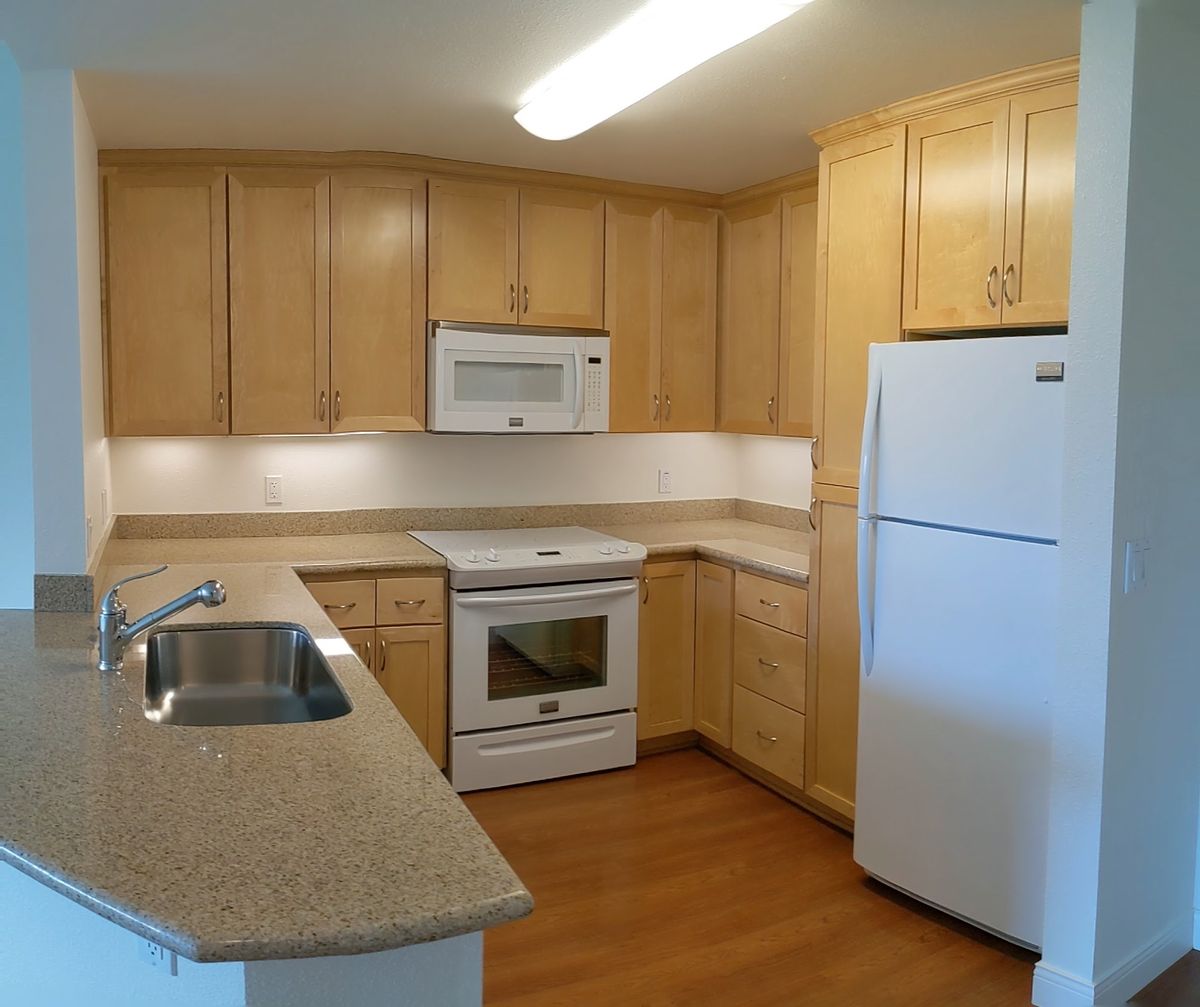 A modern kitchen with wooden cabinets, featuring a stove, microwave, refrigerator, and sink.