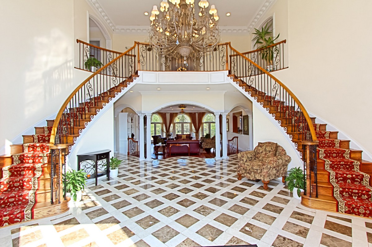 A luxurious foyer features a grand double staircase and an ornate chandelier, with elegant marble flooring and classic decor.