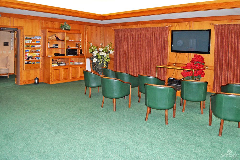 A small conference room with green chairs and wood-paneled walls, featuring a television and floral arrangement.