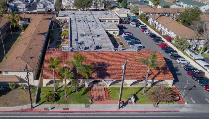 Aerial view of a building complex with a parking lot and palm trees lining the street.