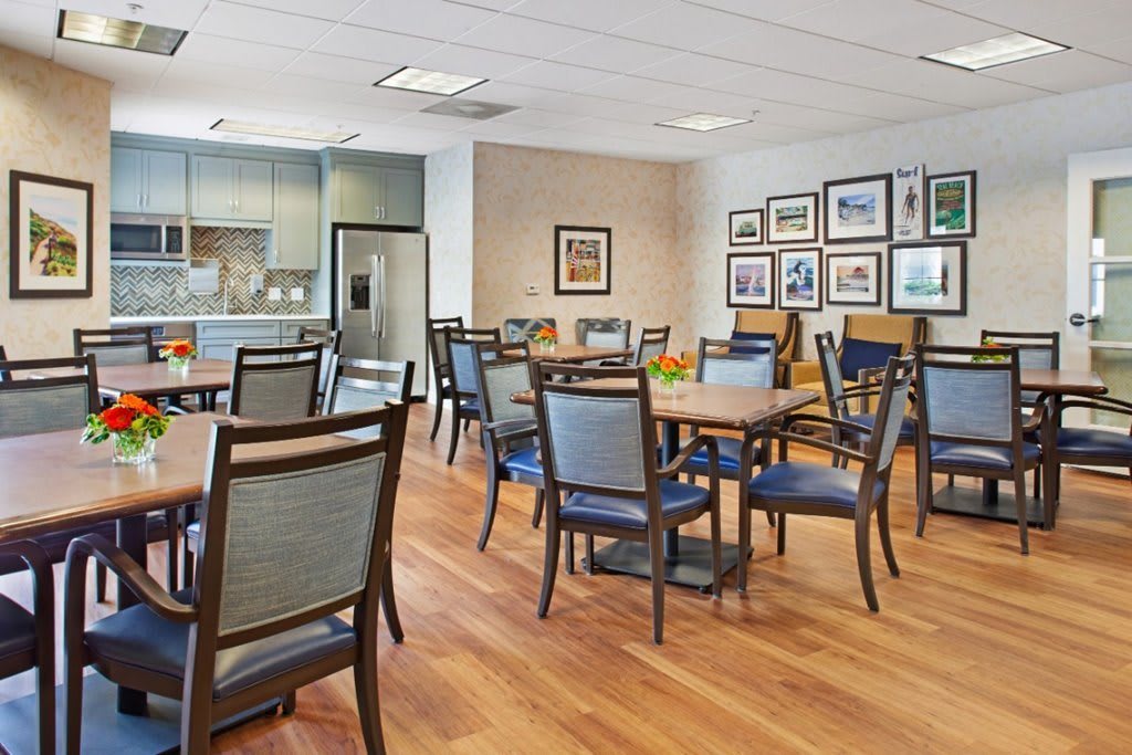 A modern dining area with multiple tables and chairs, featuring a kitchen space and decorated walls.