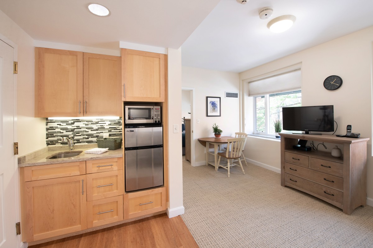 A modern, open-concept kitchen and living area featuring wood cabinetry and stainless steel appliances.