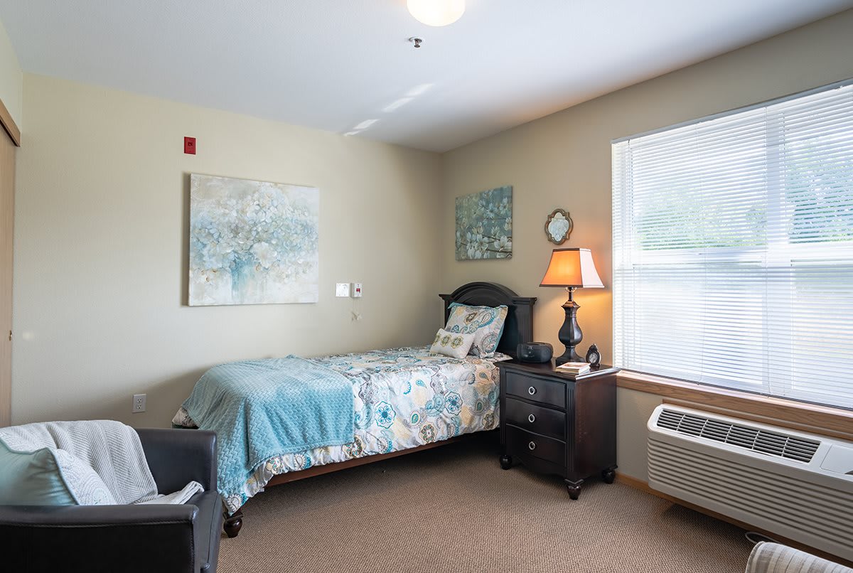 A cozy bedroom with a single bed, decorative pillows, and artwork on the beige walls.