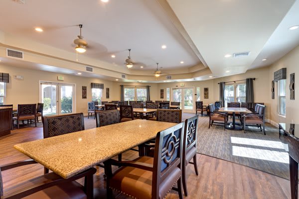 A spacious dining area with several tables and chairs, ceiling fans, and wood flooring.
