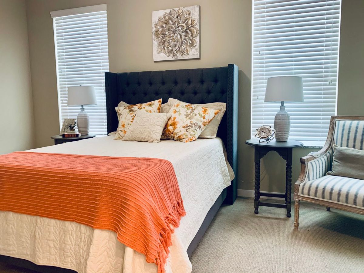 A cozy and elegantly decorated bedroom with a navy blue headboard, orange throw blanket, and matching lamps on each side.