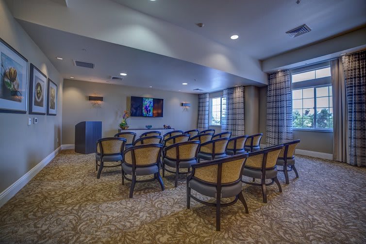 A conference room with rows of chairs facing a projector screen, illuminated by natural light from the windows.