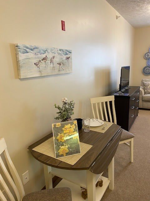 A cozy dining area with a small table set for two, adorned with flowers and artwork on the wall.