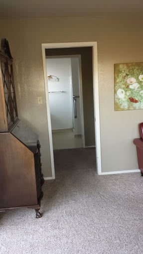 A view of a room interior featuring a doorway leading to a bathroom, with furniture and a painting on the wall.