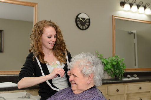 A hair stylist smiles while attending to an elderly woman in a salon setting.