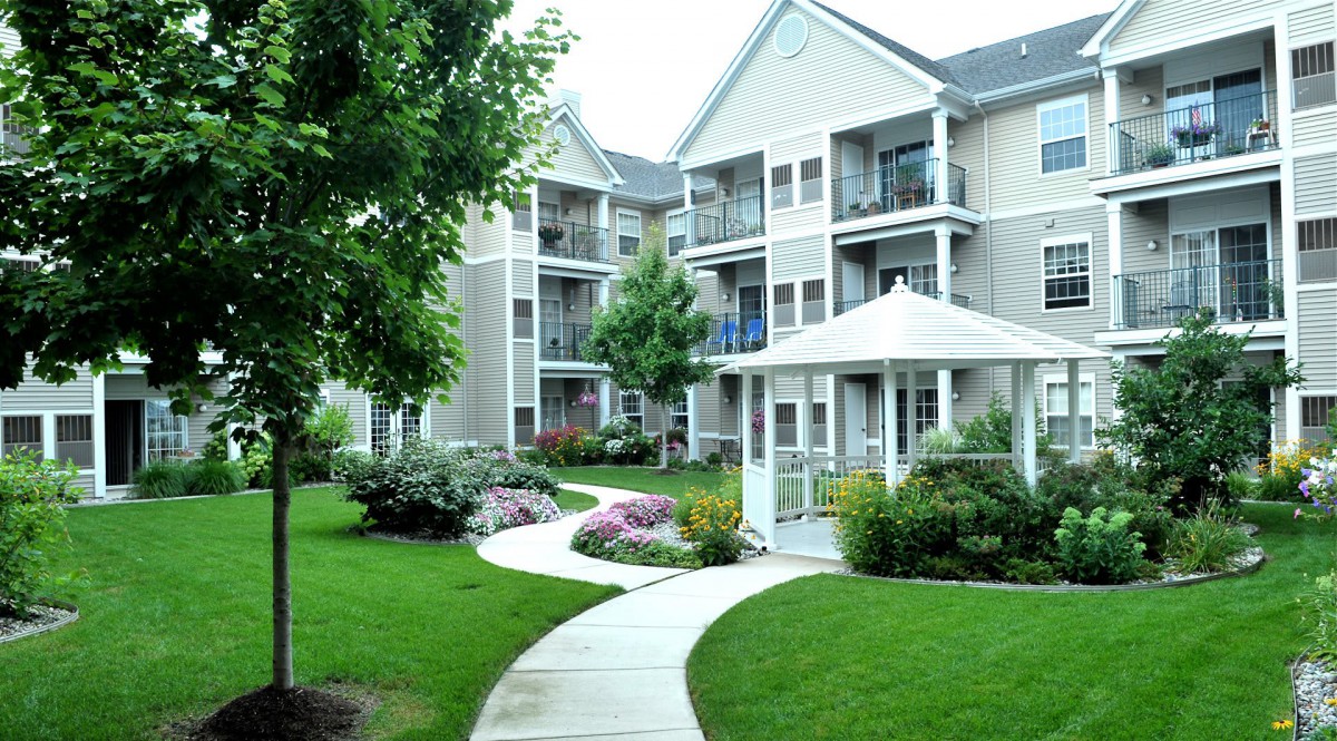 A well-maintained apartment complex with lush landscaping and a winding pathway leading to a gazebo.