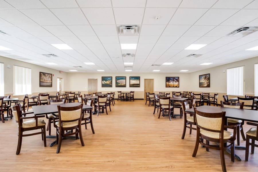 An empty dining hall with neatly arranged tables and chairs, featuring a wooden floor and wall art.