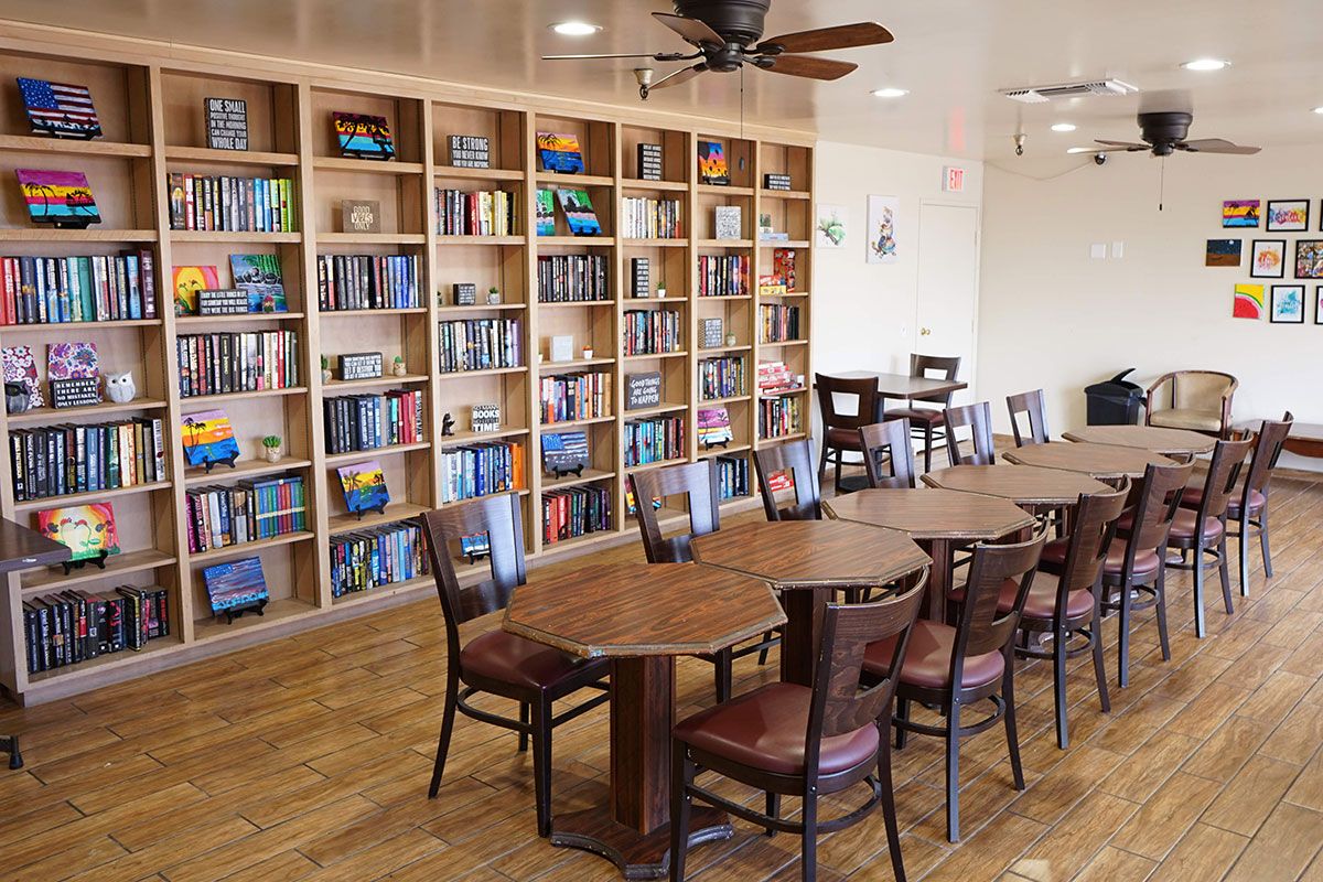A cozy library with wooden bookshelves, a long table, and chairs for reading and activities.