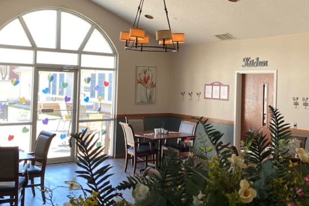 A cozy dining area with a table set for two, surrounded by plants and decorated with wall art under warm lighting.