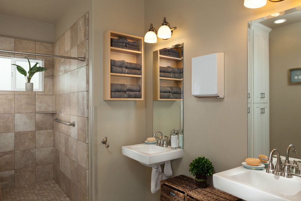 A modern bathroom with a wall-mounted sink, mirror, and built-in lighting. Shelves hold neatly folded towels, while a small plant adds a touch of greenery.