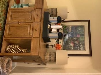 A wooden sideboard adorned with lamps and decorative items beneath a framed artwork.