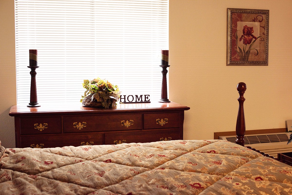 A cozy bedroom featuring a dresser adorned with a candle, flowers, and a 'HOME' sign.