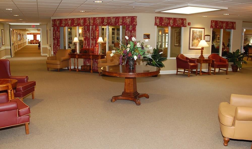 A spacious lobby area featuring a central wooden table with floral arrangements and comfortable seating.