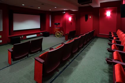 A cozy home theater with red walls and comfortable seating facing a large projection screen.