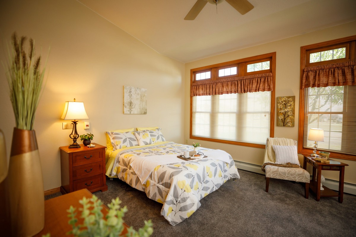 A cozy bedroom with natural light pouring through the large windows, featuring a comfortable bed and warm decor.