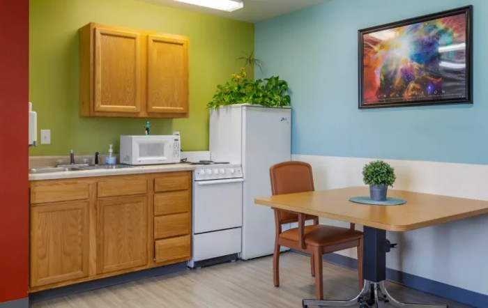A cozy kitchen area with wooden cabinets, a refrigerator, stove, and microwave, complemented by a dining table with chairs and indoor plants.