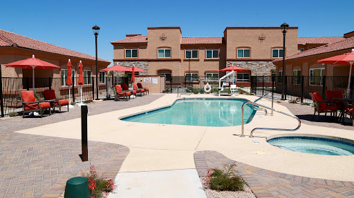 A sunny poolside area with lounge chairs and umbrellas at an apartment complex.