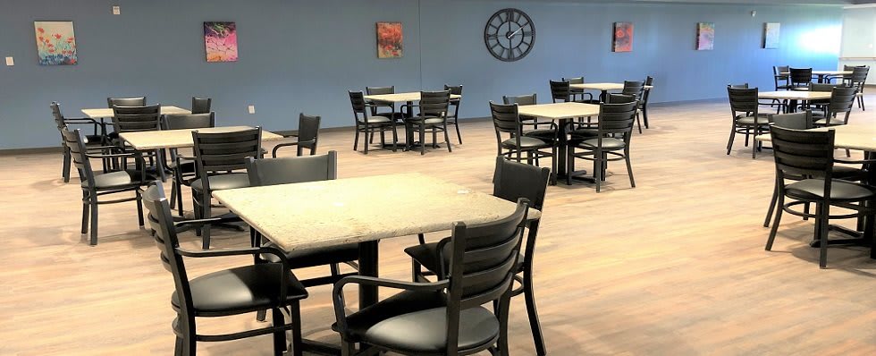 An empty dining area with wooden tables and chairs, featuring a wall clock.
