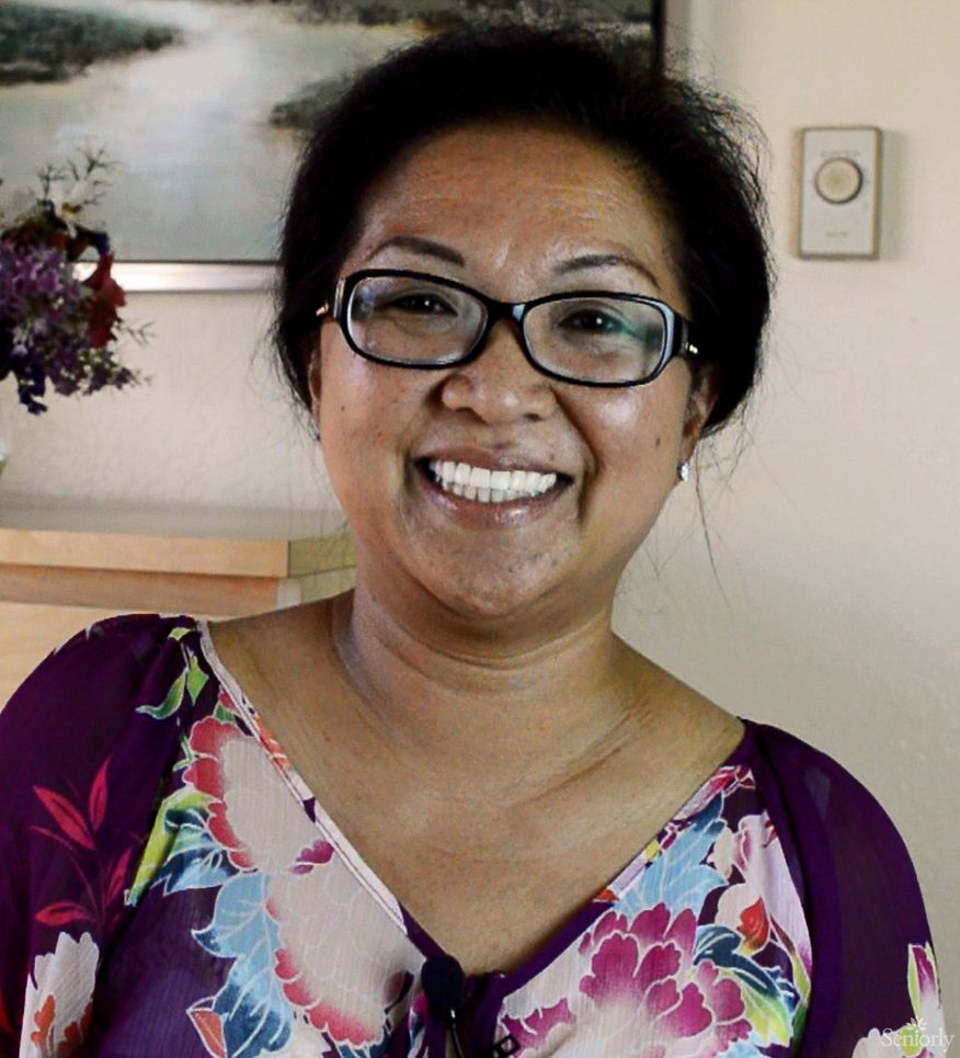 A woman wearing glasses and a floral shirt is smiling indoors.
