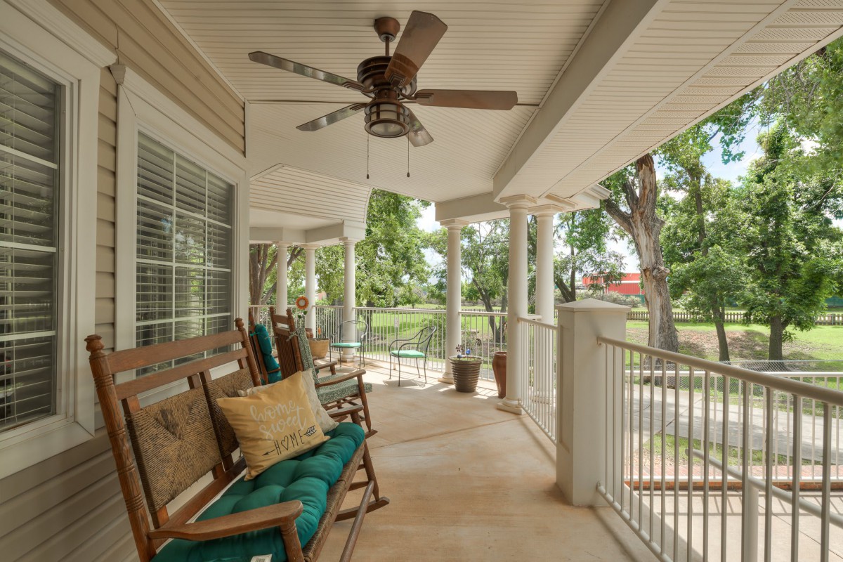 A cozy porch with rocking chairs, cushions, and a ceiling fan overlooking a lush outdoor area.